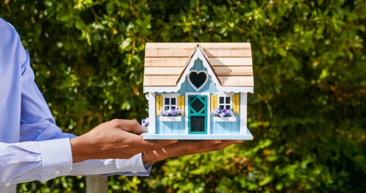 Agente imobiliário segurando uma casa de brinquedo, que simboliza a facilidade de comprar ou vender um imóvel com a ajuda de ibuyers