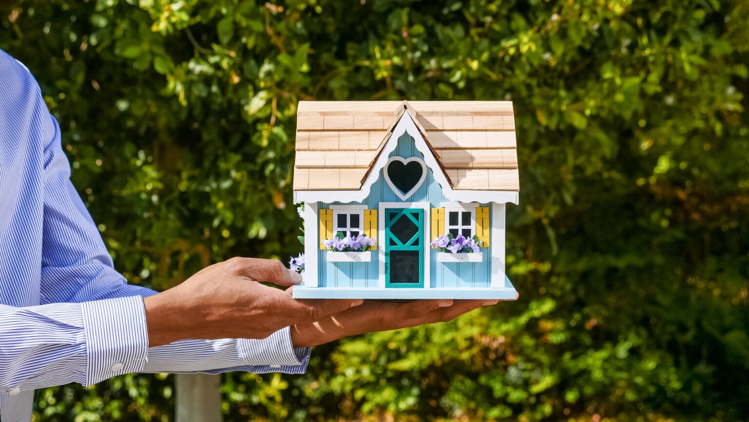 Agente inmobiliario con una casa de juguete en sus manos, simbolizando lo fácil que es comprar y vender bienes raíces con i-buyers